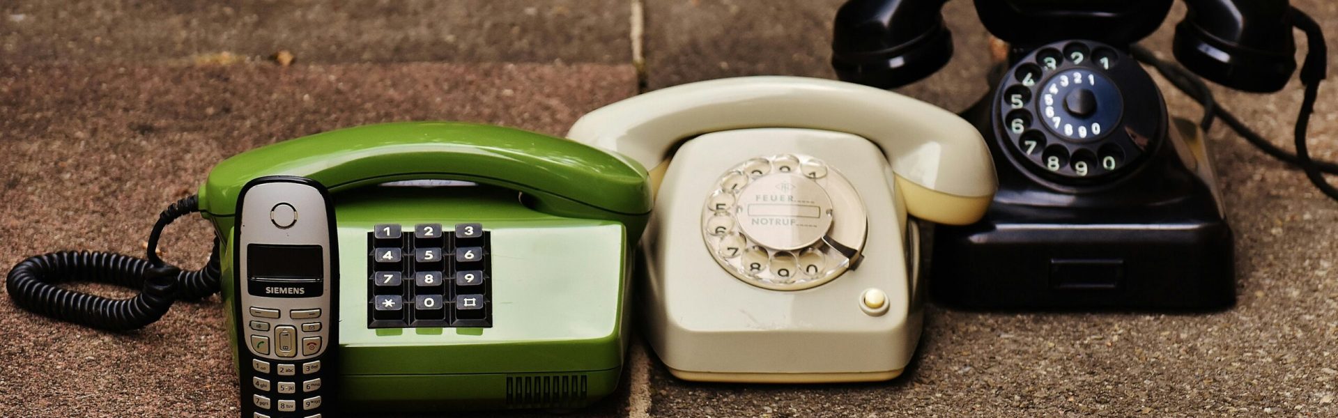 A variety of antique, vintage, and modern telephones displayed on pavement.